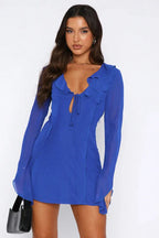 Side view of a woman in a royal blue sheer chiffon mini dress with long bell sleeves.