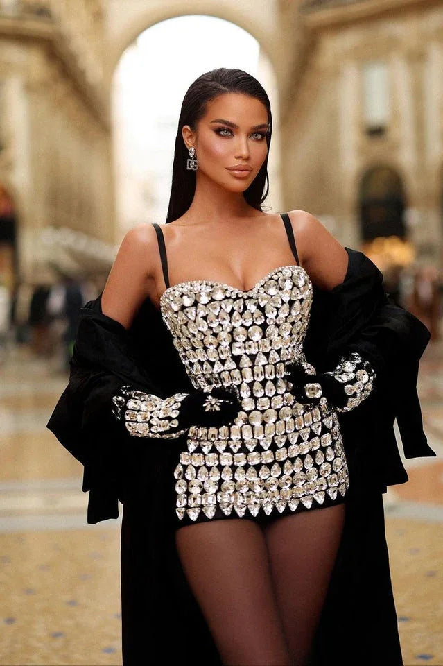 Woman wearing a crystal-embellished strapless mini dress, black gloves, and a black coat draped over her shoulders.