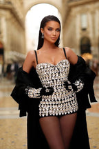 Woman wearing a crystal-embellished strapless mini dress, black gloves, and a black coat draped over her shoulders.