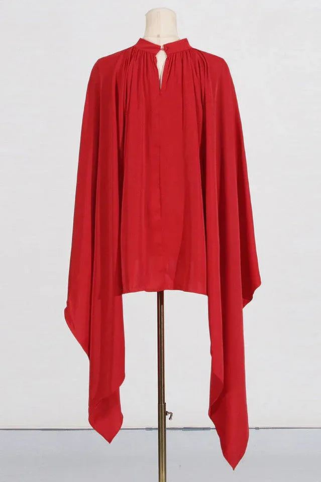 Back view of the red crepe jumpsuit displayed on a mannequin, showing the full length of the cape sleeves.