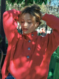 Woman wearing a coral knit sweater with her hands in her hair, showcasing the button detail and ribbed texture.