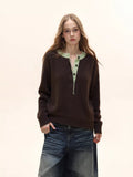 Woman wearing a brown long-sleeved knit sweater with a light green contrast neckline and button-up placket, paired with distressed denim jeans.