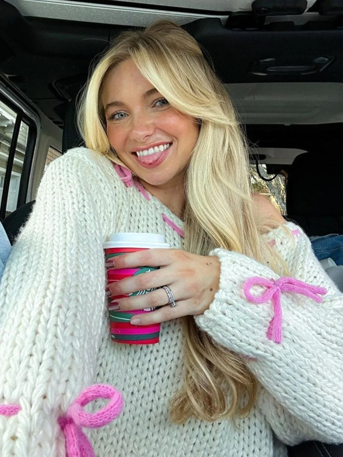 Woman wearing a chunky cream knit sweater with pink stitching details, holding a bouquet of flowers.