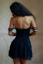 Woman wearing a black strapless mini dress with ruffle detailing and off-the-shoulder straps, back view.