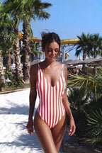 Woman wearing a red and white striped one-piece swimsuit walking on sand