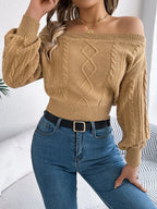Woman wearing a tan off-the-shoulder cable knit cropped sweater with balloon sleeves and blue jeans.