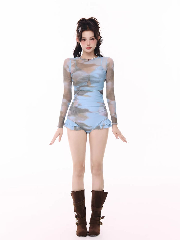Full-body front view of a woman in a blue and grey cloud print swimsuit with a sheer overlay and ruffled hem.