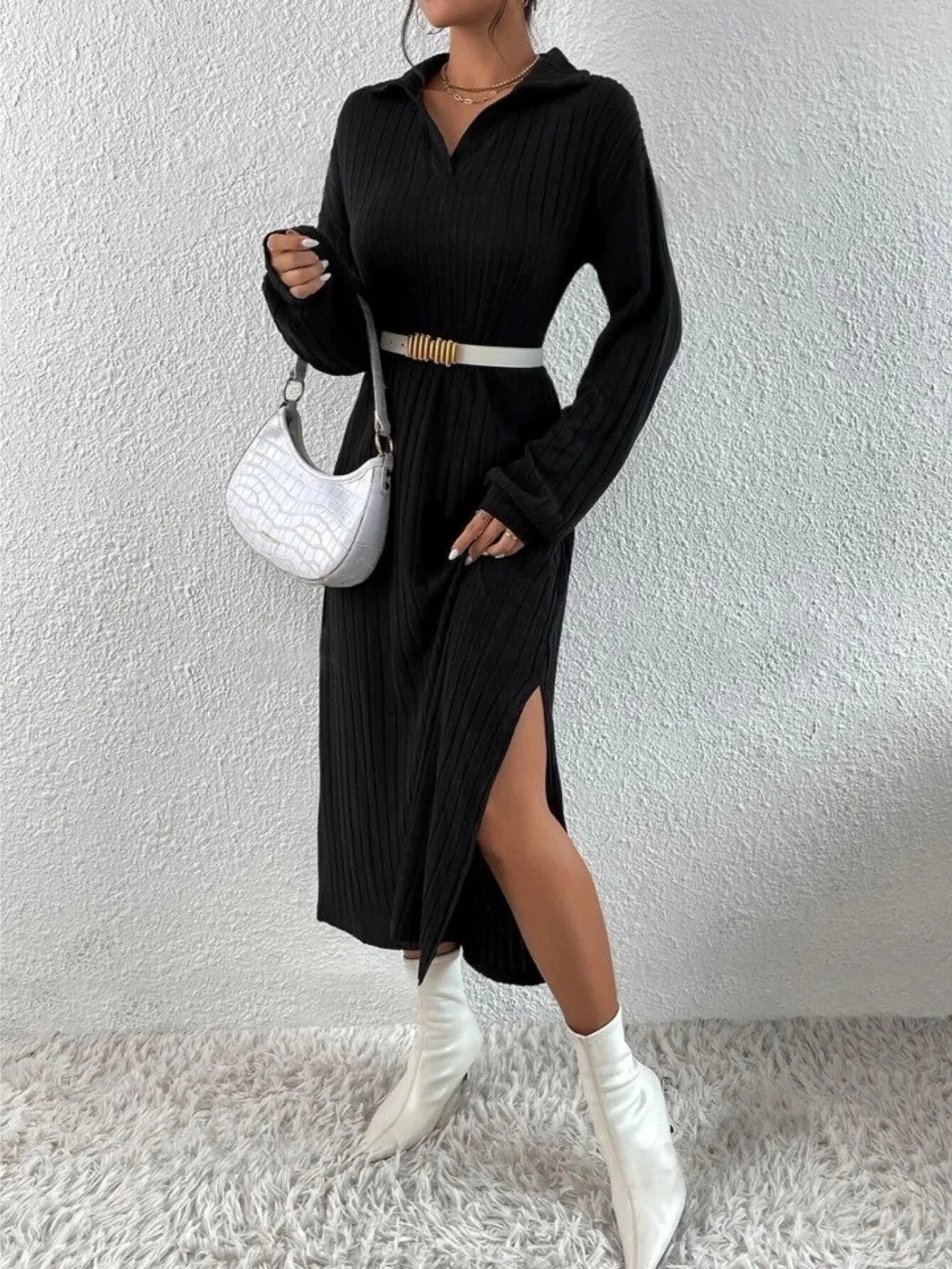 Full body shot of a model in a black ribbed knit midi dress, styled with a white belt and handbag.