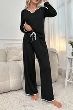 Woman in black long-sleeve pajama top and pants with white piping detail standing in a living room.