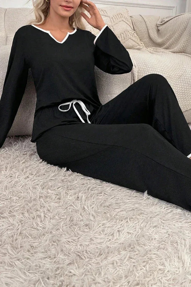 Woman in black long-sleeve pajama top and pants with white piping detail sitting on a fluffy rug.