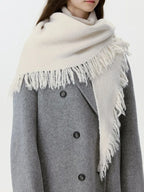 Side view of a woman wearing a cream-colored knit scarf with fringe detail and a grey coat.