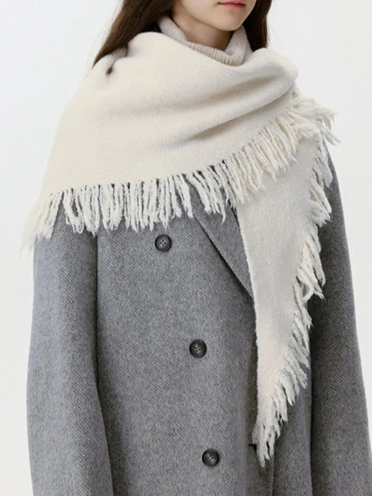 Side view of a woman wearing a cream-colored knit scarf with fringe detail and a grey coat.