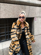 Woman in a faux fur tiger stripe coat and black pants posing outdoors.