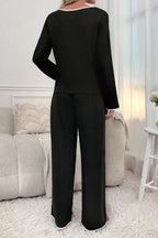 Back view of woman in black long-sleeve pajama top and pants with white piping detail.