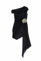 Black one-shoulder asymmetrical mini dress with ruched detailing, draped chiffon overlay, and a floral embellishment, shown flat.