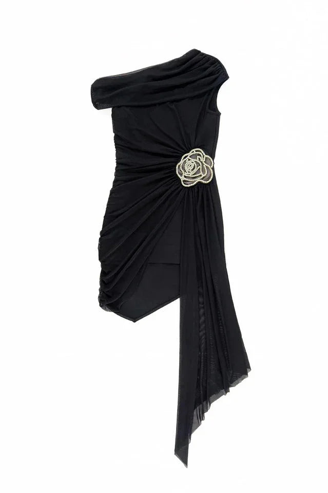 Black one-shoulder asymmetrical mini dress with ruched detailing, draped chiffon overlay, and a floral embellishment, shown flat.