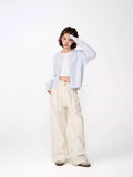 Full body shot of a woman wearing a light blue cropped knit cardigan and cream wide-leg pants.