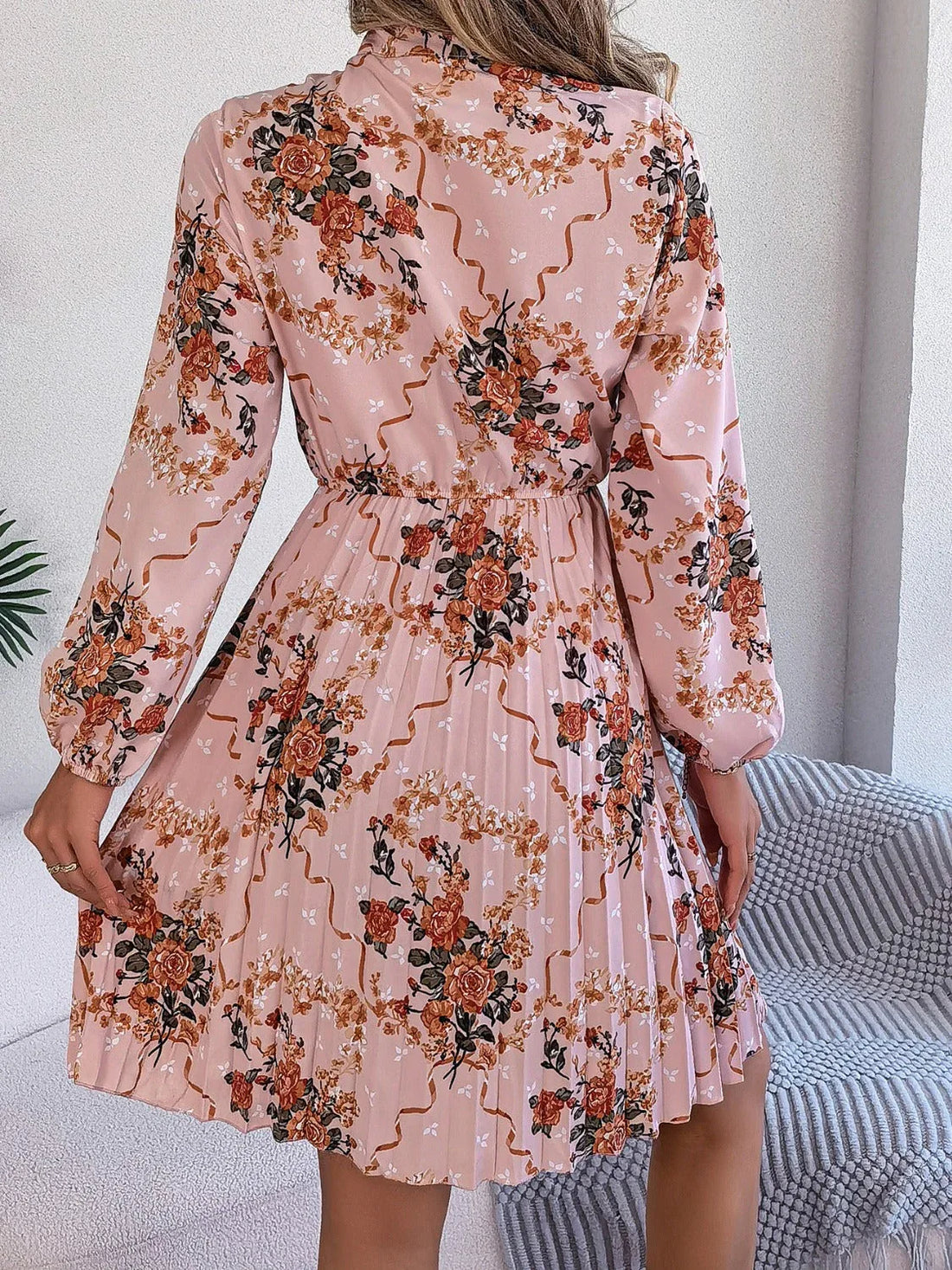 Woman wearing a pink floral print midi dress with a bow neckline and pleated skirt