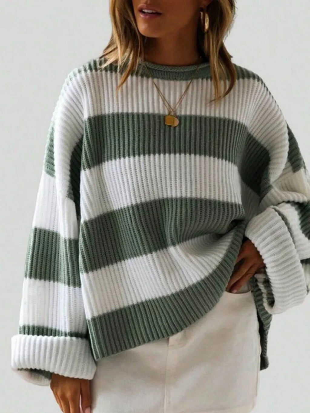 Woman wearing a green and white striped oversized knit sweater with crew neck and long cuffed sleeves.