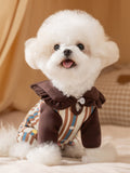 Small white dog wearing brown and beige striped pajamas with a ruffled collar.