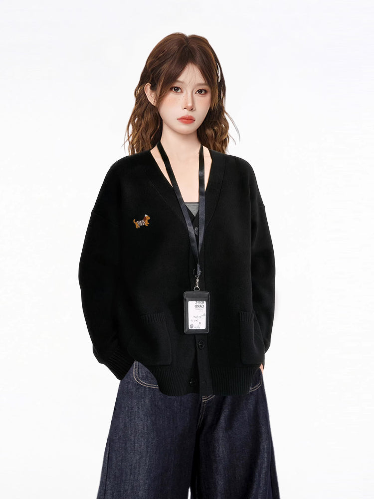 Close-up of the woman's upper body, showcasing the details of the black knit cardigan, including the V-neckline, button-down closure, and the embroidered dachshund graphic.