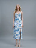 Woman wearing a white slip dress with a blue floral print, spaghetti straps, cowl neckline, and a high side slit.