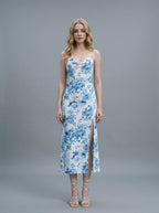 Woman wearing a white slip dress with a blue floral print, spaghetti straps, cowl neckline, and a high side slit.