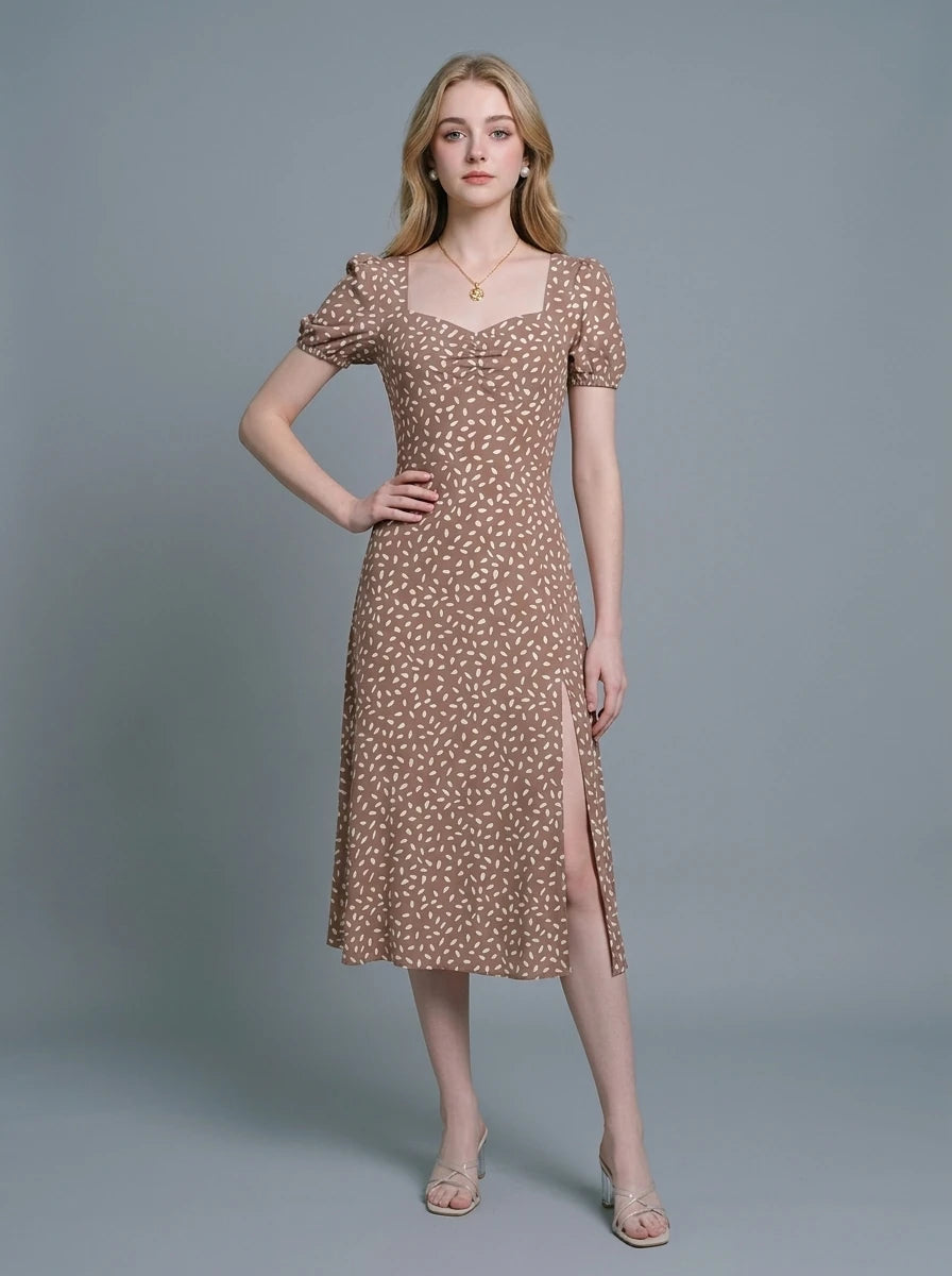Woman wearing a brown midi dress with a white abstract print, puff sleeves, sweetheart neckline, and a high side slit.