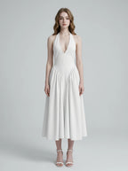 Woman wearing a white halter neck midi dress with a V-neckline and flared skirt.