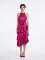 Woman wearing a fuchsia satin halter neck tiered midi dress with a self-tie belt