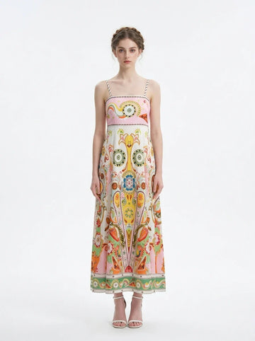 Woman wearing a long, printed sundress with spaghetti straps and a square neckline, standing against a white background.