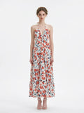 Woman wearing a white maxi dress with an orange and blue floral print, halter neckline, and tiered skirt.