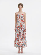 Woman wearing a white maxi dress with an orange and blue floral print, halter neckline, and tiered skirt.
