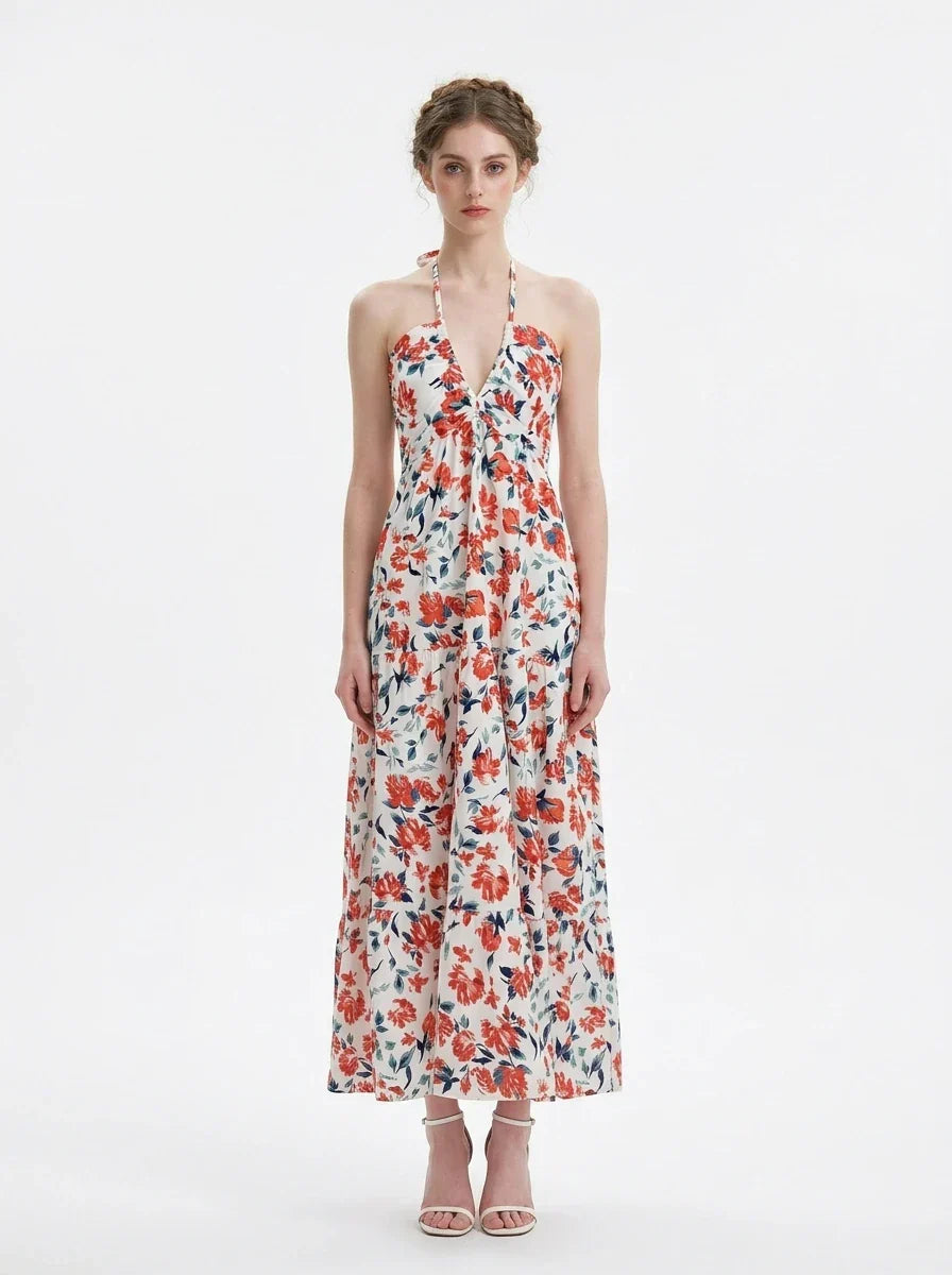 Woman wearing a white maxi dress with an orange and blue floral print, halter neckline, and tiered skirt.