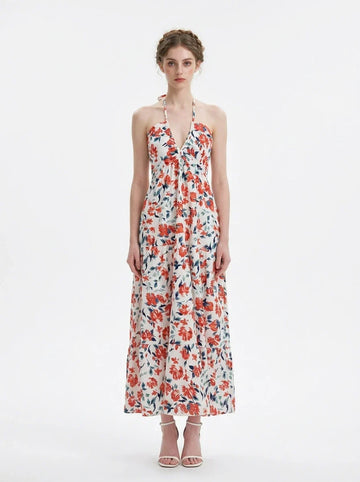Woman wearing a white maxi dress with an orange and blue floral print, halter neckline, and tiered skirt.