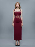 Woman wearing a long burgundy dress with a square neckline and lace detailing on the bodice.