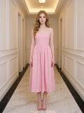 Woman wearing a pink midi dress with spaghetti straps and a square neckline, standing in a hallway.