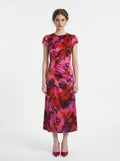 Woman in a pink and red floral print satin ruched midi dress with cap sleeves.