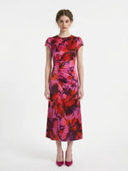 Woman in a pink and red floral print satin ruched midi dress with cap sleeves.