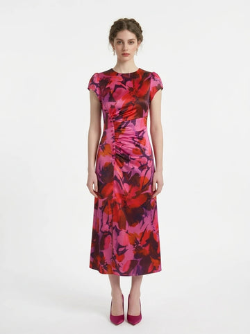 Woman in a pink and red floral print satin ruched midi dress with cap sleeves.