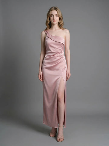 Woman wearing a dusty rose satin one-shoulder maxi dress with a high slit, standing against a grey background.