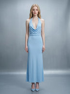 Woman in a light blue maxi halter dress with a draped cowl neckline and open back with pearl detailing.