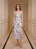 Woman wearing a white midi dress with a blue floral print and tie shoulder straps, standing in a hallway.