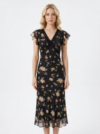 Woman wearing a black floral print midi dress with flutter sleeves and lace trim.