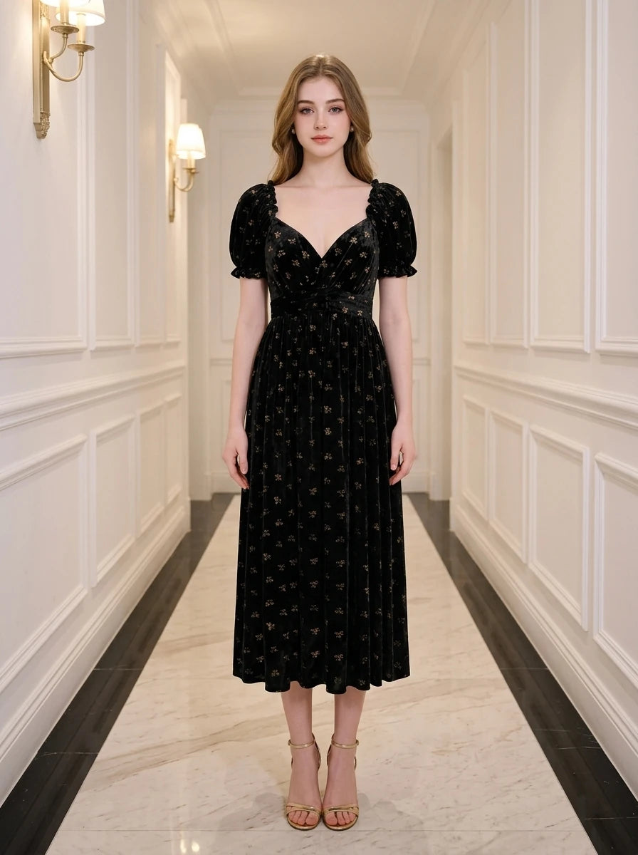 Woman wearing a black floral burnout velvet midi dress with puff sleeves and a sweetheart neckline, standing in a hallway.