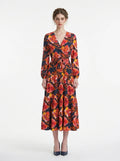 Woman wearing a navy blue long-sleeved midi dress with a bold red and yellow floral print and a V-neck wrap design, cinched at the waist with a matching belt.