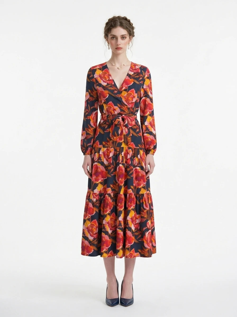 Woman wearing a navy blue long-sleeved midi dress with a bold red and yellow floral print and a V-neck wrap design, cinched at the waist with a matching belt.