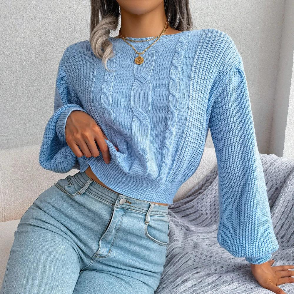 Woman wearing a light blue cable knit cropped sweater with balloon sleeves and light wash jeans, seated on a couch.