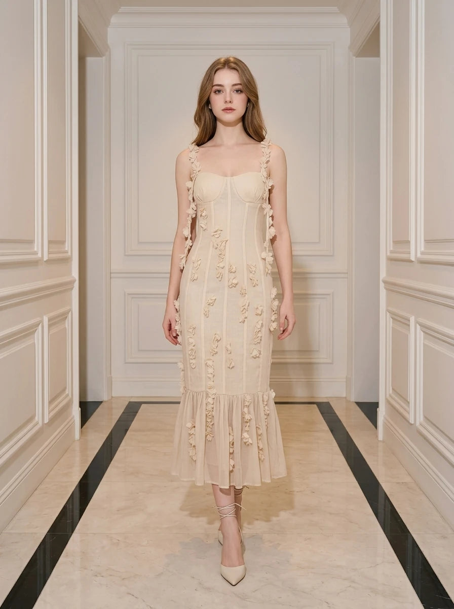Woman wearing a cream-colored midi dress with 3D floral embellishments and a ruffled hem, standing in a hallway.