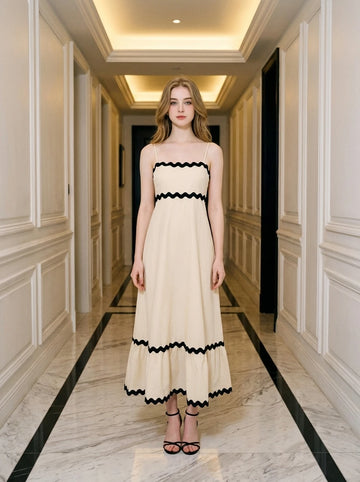 Woman standing in a hallway wearing a cream-colored midi dress with black zig-zag trim.